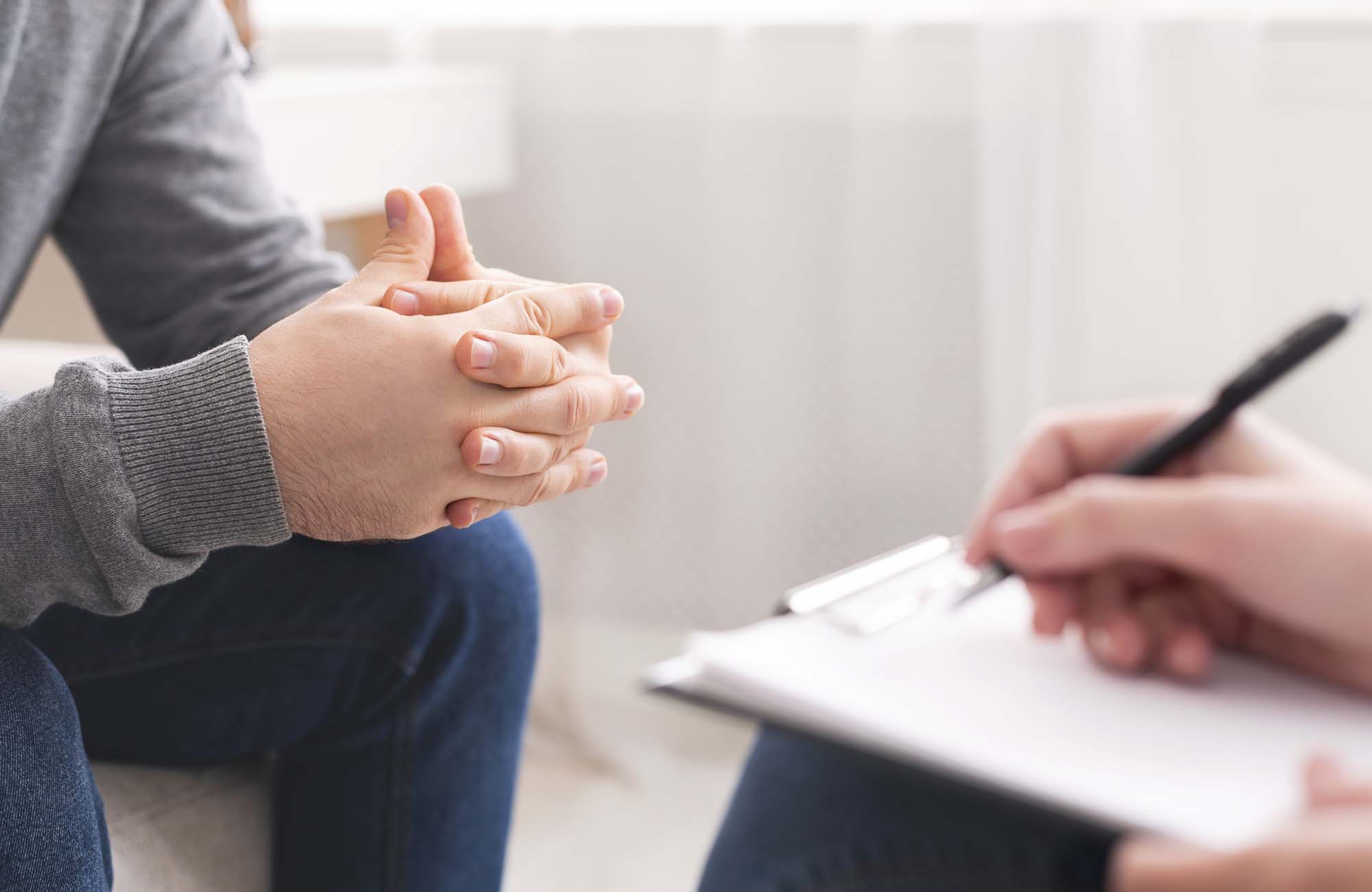 Therapist writing notes during counseling session with single man sitting on couch, panorama, empty space